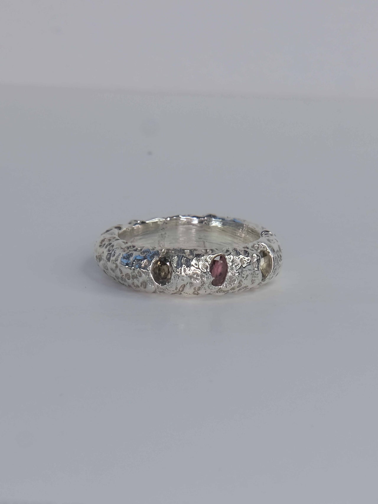 Handgefertigter Ring aus 925 Sterling-Silber strukturierter Oberfläche, durch Sandguss gefertigt, und drei grünen und roten Saphiren – designed und made in Berlin.