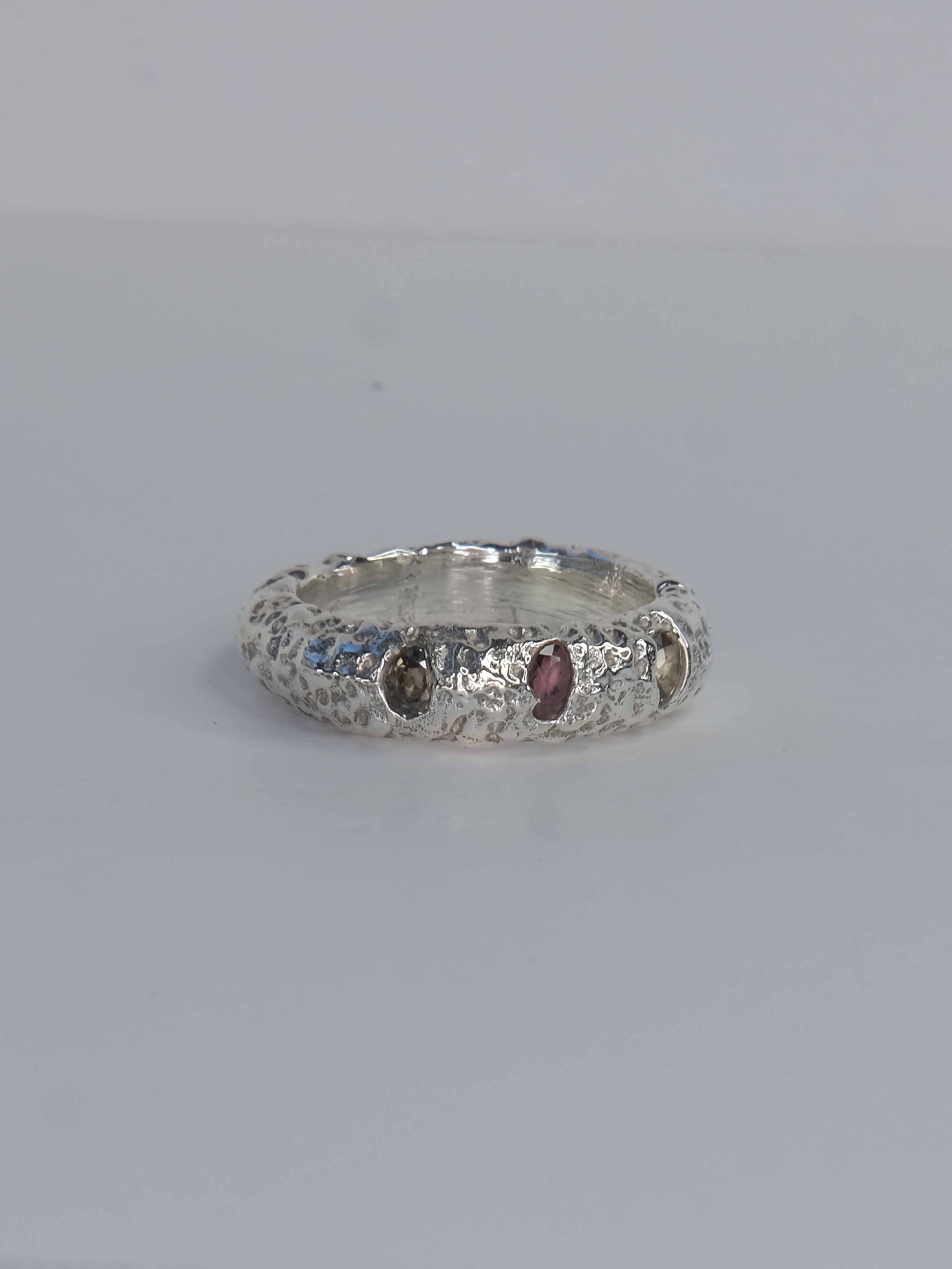 Handgefertigter Ring aus 925 Sterling-Silber strukturierter Oberfläche, durch Sandguss gefertigt, und drei grünen und roten Saphiren – designed und made in Berlin.