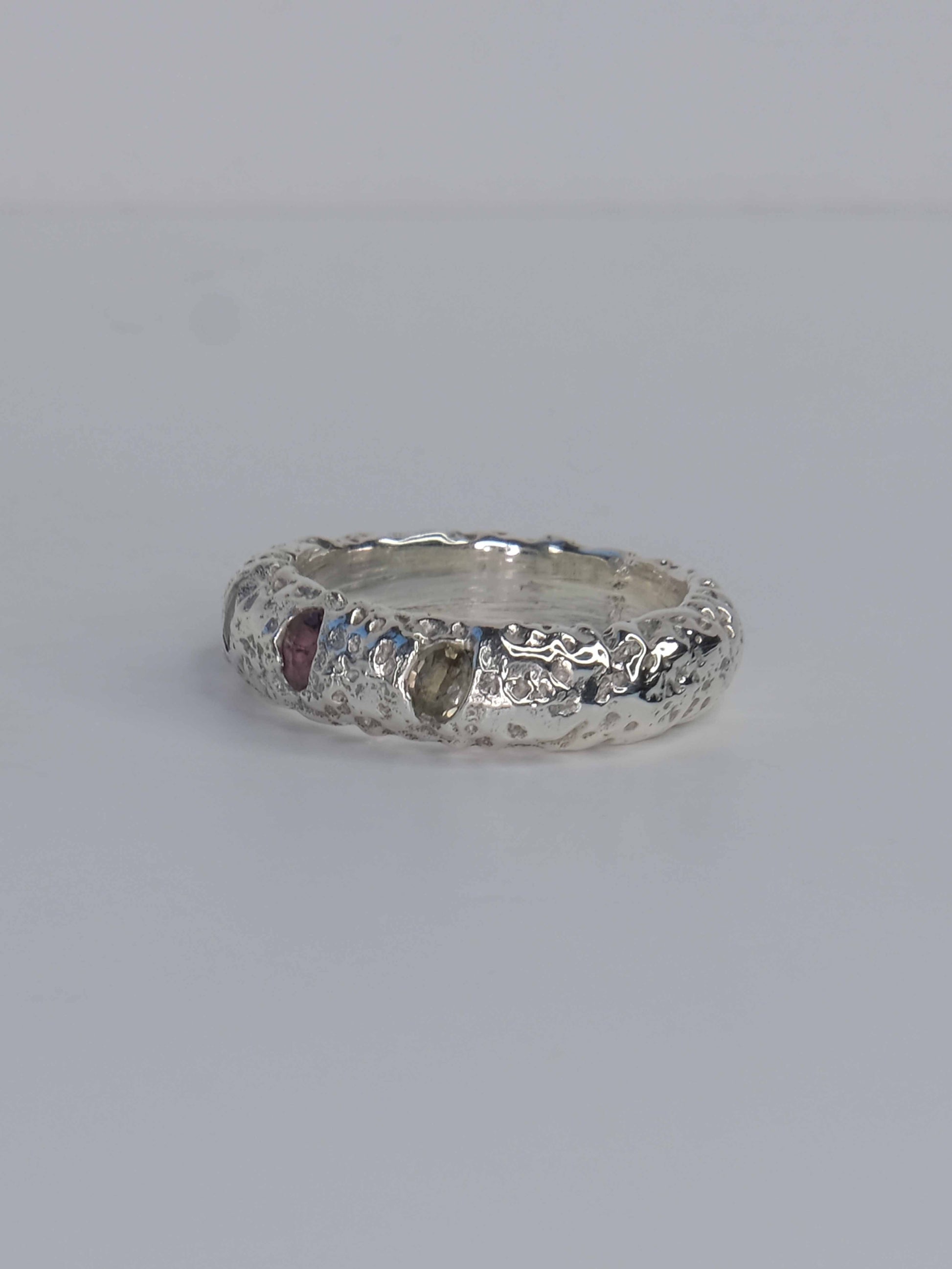 Handgefertigter Ring aus 925 Sterling-Silber strukturierter Oberfläche, durch Sandguss gefertigt, und drei grünen und roten Saphiren – designed und made in Berlin.